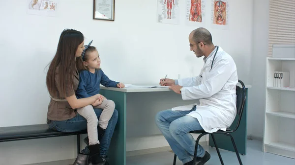 Pediatra rellenando formulario médico mientras la madre con su hija pequeña describe su problema — Foto de Stock