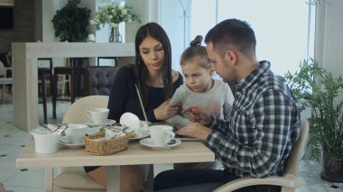 Dizüstü bilgisayar kullanarak, sohbet ve kafe ya da Restoran gülümseyen genç ailesi.