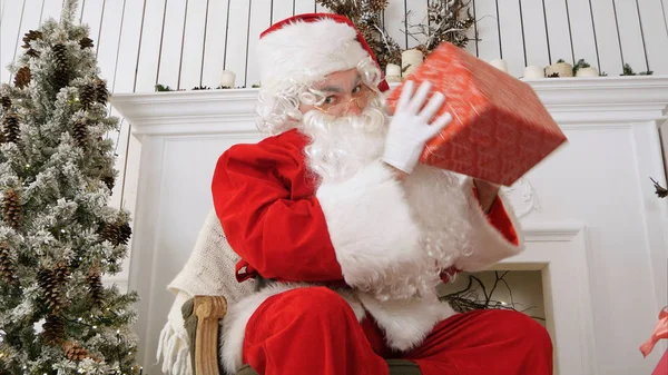 Papai Noel olhando para a câmera e provocando com um presente — Fotografia de Stock