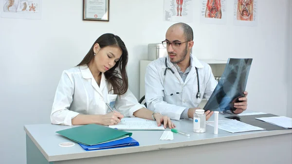 Médico masculino enseñando a su aprendiz femenina sin experiencia cómo analizar rayos X — Foto de Stock