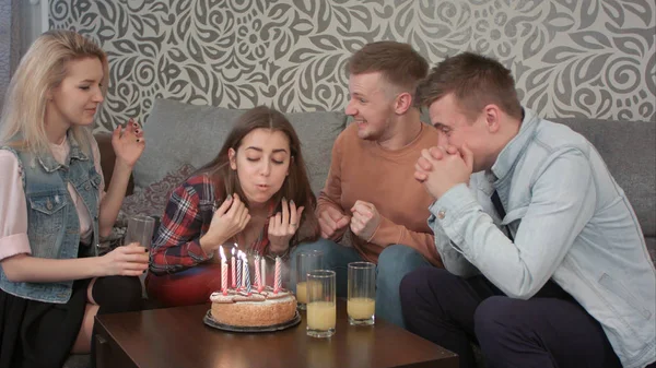 Attractive teen girl celebrates her birthday with friends at home and blows out the candles on cake and drinks orange juce