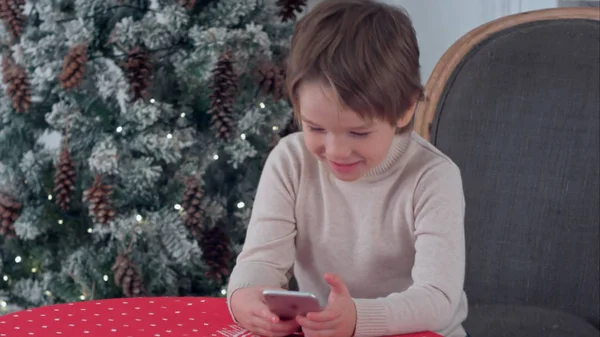 Μικρό ευτυχισμένο αγόρι, χρησιμοποιώντας έξυπνο τηλέφωνο στο σπίτι διακοσμημένα για τα Χριστούγεννα — Φωτογραφία Αρχείου