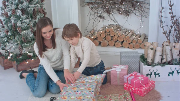 Happy mother and her little son wrapping up Christmas gifts at home