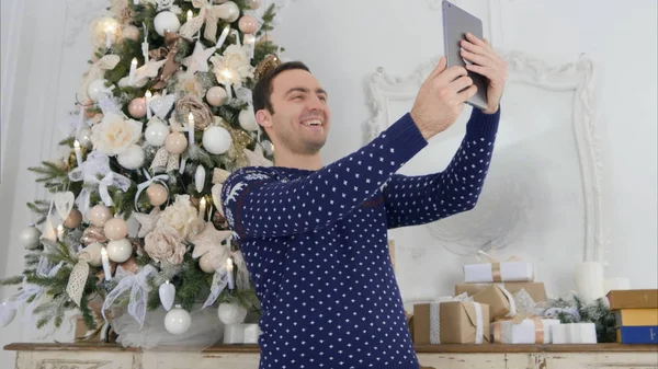 Joven en un suéter de punto tomando selfies en una tableta netx al árbol de Navidad — Foto de Stock