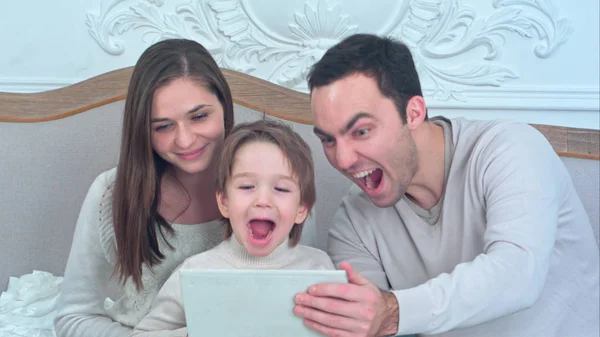 Молода щаслива сім'я дивиться свої фотографії на планшет і сміється — стокове фото