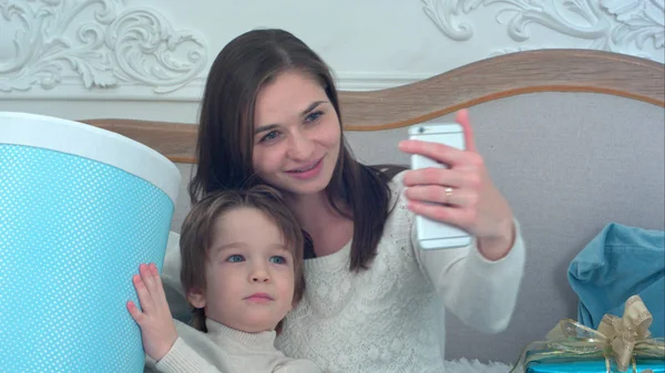 Young mother and happy son holding Christmas presents taking selfies with phone