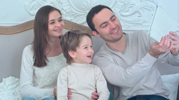 Счастливая молодая семья делает селфи на диване с планшетом — стоковое фото