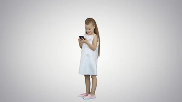 Urocza dziewczynka uśmiechnięta i korzysta z telefonu komórkowego na białym tle — Zdjęcie stockowe