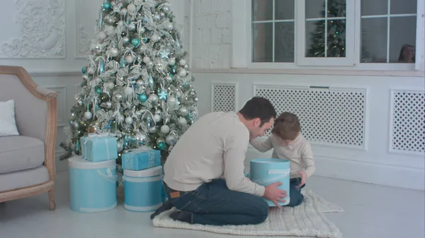 Apa és fia boldog megnyitása bemutatja a karácsonyfa mellett ülő mosolyogva — Stock Fotó