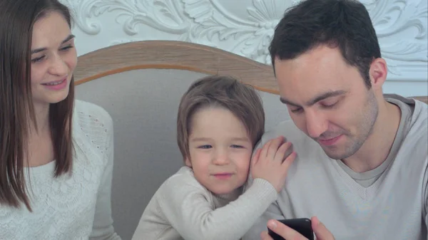Glad ung familj sitter i soffan med far använder telefonen — Stockfoto