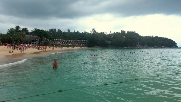 PHUKET, TAILANDIA - 20 ENE 2017: Muchas tumbonas están en la playa de arena y la gente nada en el mar en el día nublado — Foto de Stock