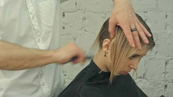 Cliente sorridente sentado em um salão de cabeleireiro enquanto o cabeleireiro está penteando seu cabelo. Foco no cliente — Fotografia de Stock