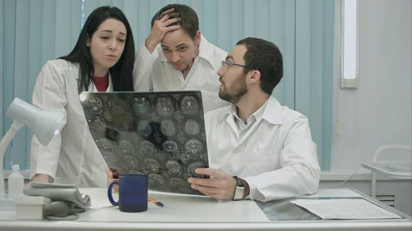Trío de médicos jóvenes asustados revisando pacientes escáner de cabeza — Foto de Stock