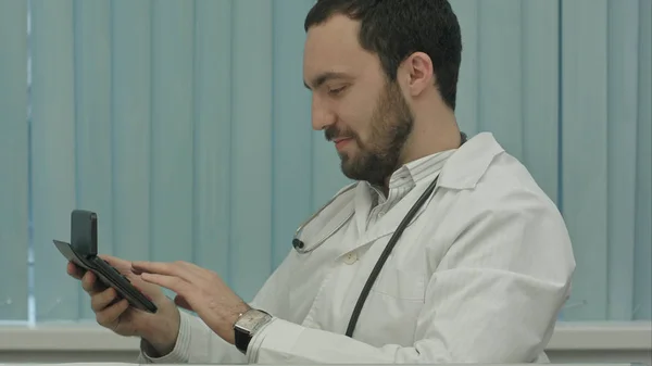 Bärtiger Arzt mit Taschenrechner. Berechnung des Preises vornehmen und zufrieden damit sein — Stockfoto