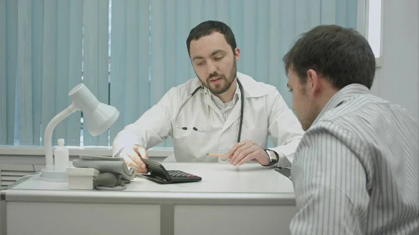 Male bearded doctor in clinic calculate high price for treatment. — Stock Photo, Image