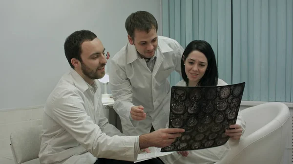 Два врача в хорошем настроении анализируют результаты пациента для диагностики заболевания, затем приходят интерны с рентгеном — стоковое фото