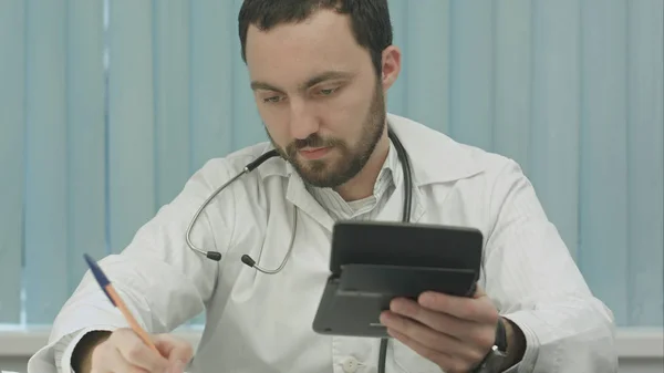 年轻男医生用计算器进行计算和做笔记 — 图库照片
