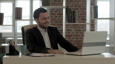 Ofisinde dizüstü bilgisayarı olan gülümseyen bir adam.