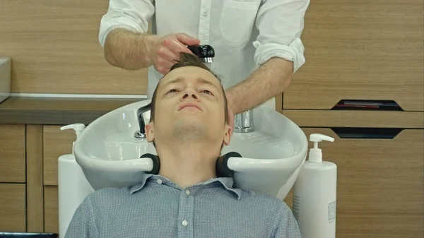 Schöner Mann, der sich im Friseursalon die Haare waschen lässt. Junger Mann liegt mit geschlossenen Augen in Schönheitssalon. — Stockfoto