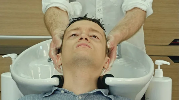 Professional hairdresser washing hair to her handsome client.