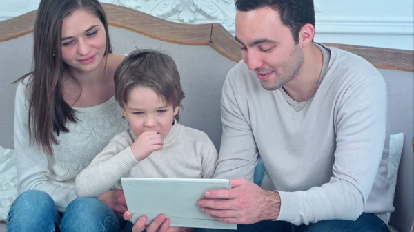 Папа, мама и их маленький сын веселятся, играя вместе с планшетом, сидя на диване — стоковое фото