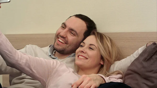 Szczęśliwa para co grymasy i biorąc selfie na łóżku — Zdjęcie stockowe