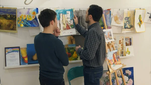 Two young men discussing paintings drawn by art students