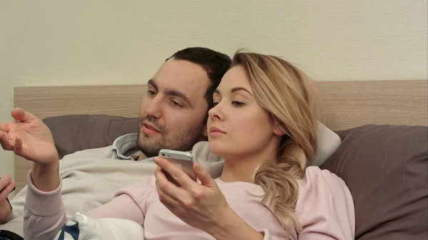 Esposa y marido viendo película divertida, discutiendo, mujer usando teléfono inteligente — Foto de Stock