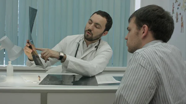 Male bearded doctor in clinic show x-rays to male client. — Stock Photo, Image