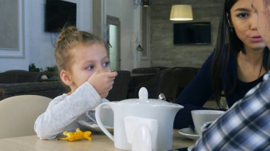 Kafede güzel ailesiyle birlikte oturan çay içme küçük sarışın kız.