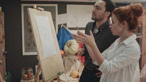 Kunstlehrerin und ihr Lehrling diskutieren Gesichtsproportionen auf Staffelei — Stockfoto