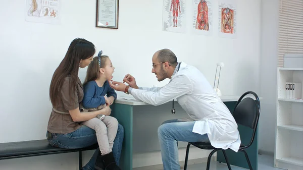 男性の小児科医が母親と一緒に座っている少女の喉を調べる — ストック写真