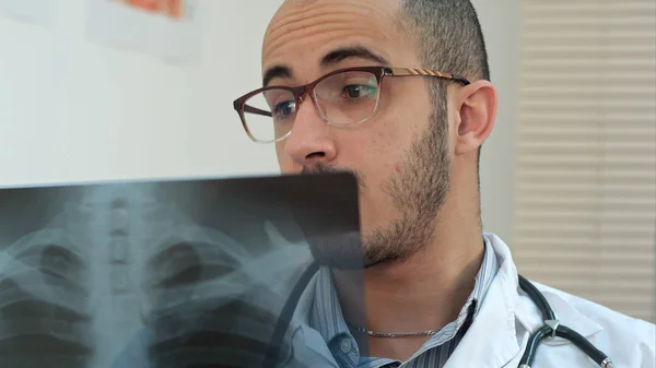 Young male doctor in glasses carefully analyzing xray image — Stock Photo, Image