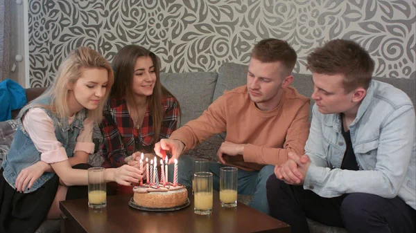 Teen boy lighting a birthday candle on cake with friends at home