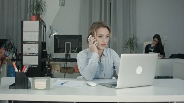 Dizüstü bilgisayarda çalışan ve telefon görüşmesi cevap genç ofis Sekreteri