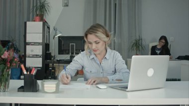 Dizüstü bilgisayar ve onun Ofis Masası, not almak yazarak gülümseyen kadın