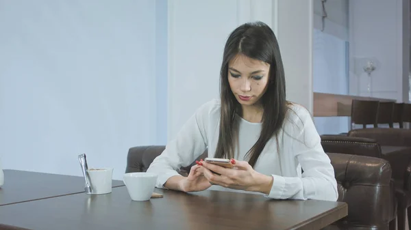 Hermosa mujer joven mensajes de texto en el teléfono inteligente en un café — Foto de Stock