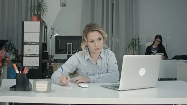 忙时她使用平板电脑的同事办公室在笔记本电脑上工作的年轻女子 — 图库照片