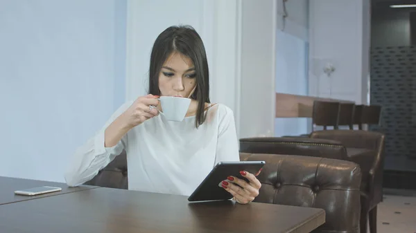 Jovem mulher usando tablet digital enquanto bebe café ou chá em um café — Fotografia de Stock