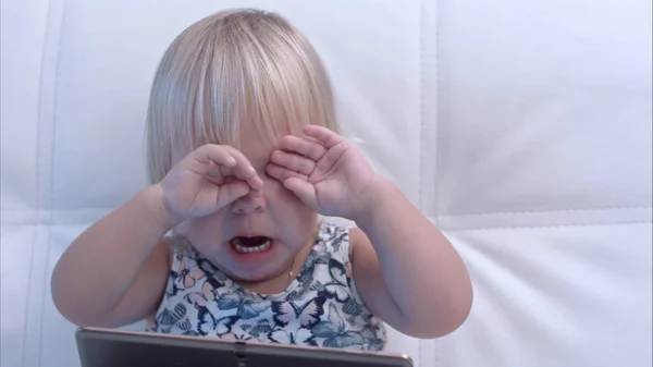 Niña con tableta frotándose los ojos después de llorar — Foto de Stock