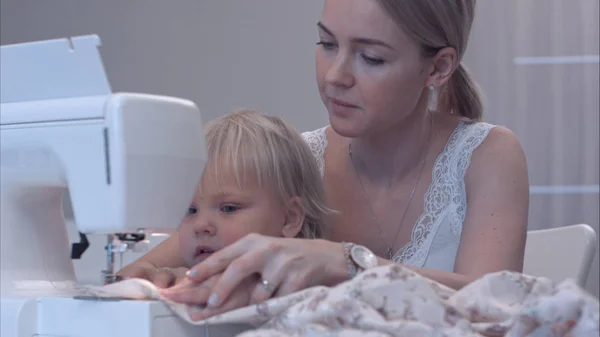 Küçük çocuk annesi dikiş makinesi kullanarak yeni bilgi öğrenir