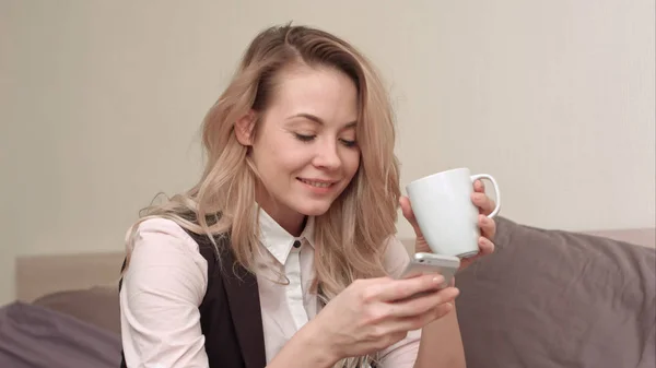 Kobieta za pomocą telefonów komórkowych w łóżku w nocy i picie herbaty — Zdjęcie stockowe