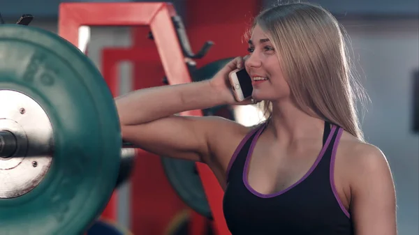 Smiling fit woman talking on the phone in the gym weight room