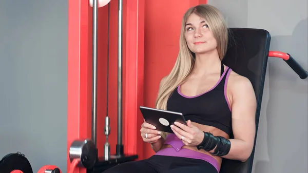Leende kvinna använder tablett medan du gör ben övningar i gymmet — Stockfoto