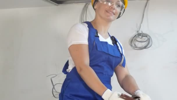 Улыбающаяся женщина-строитель в каскадных шлифовальных стенах в помещении на стройплощадке — стоковое видео