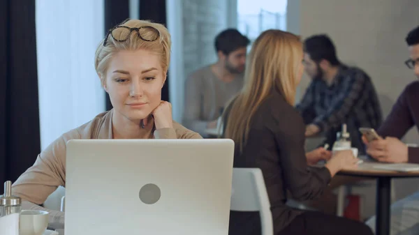 Retrato de sonriente mujer de negocios bastante joven posponiendo gafas sentado en la cafetería woth portátil — Foto de Stock