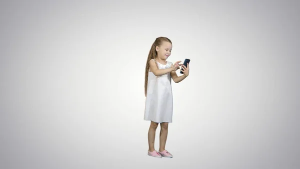 Cute little girl uses a smartphone and laugh on white background — Stock Photo, Image