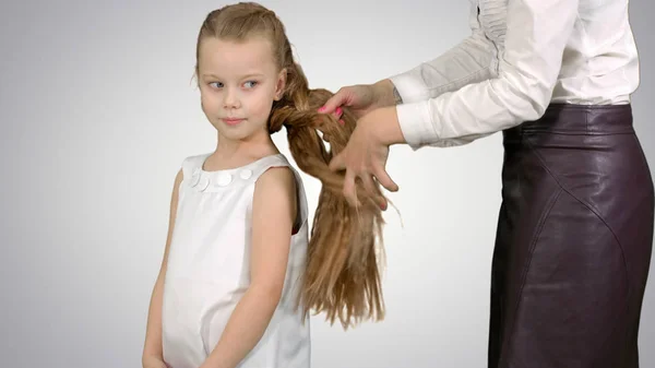 Mãe faz penteado filha no fundo branco — Fotografia de Stock