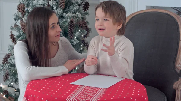 A happy boy and his mother fantasizing what to write in a letter to Santa