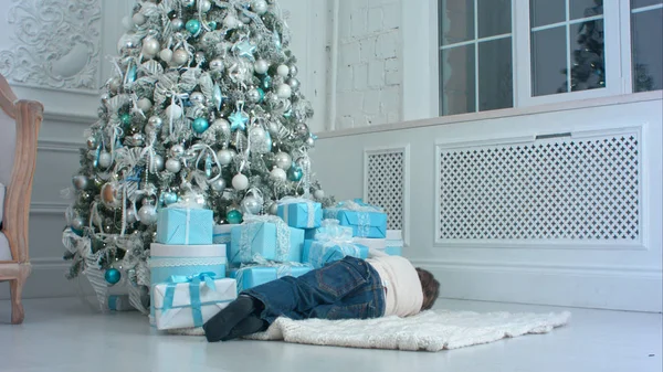 Kleiner Junge täuscht vor, auf dem Teppich neben dem Weihnachtsbaum zu schlafen — Stockfoto